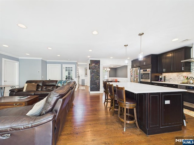 kitchen featuring crown molding, appliances with stainless steel finishes, light countertops, open floor plan, and backsplash