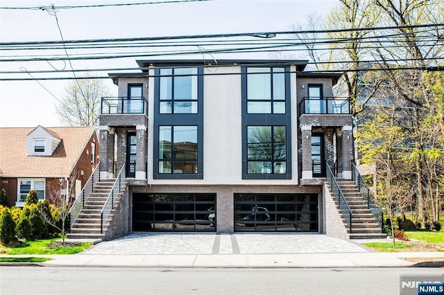 view of front of house with an attached garage, decorative driveway, a balcony, and stairway