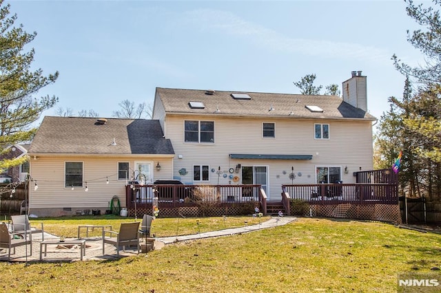 rear view of property with a lawn, a wooden deck, a chimney, and an outdoor fire pit