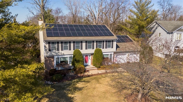 view of front facade with driveway, a chimney, solar panels, and a garage