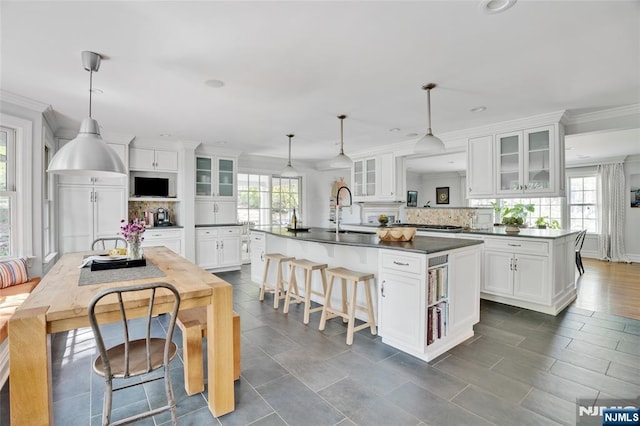 kitchen featuring a kitchen island with sink, dark countertops, decorative backsplash, and a sink