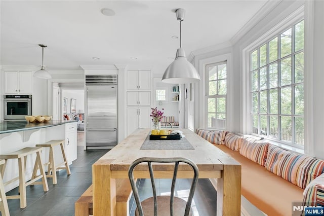 kitchen featuring pendant lighting, ornamental molding, a breakfast bar, stainless steel appliances, and white cabinetry