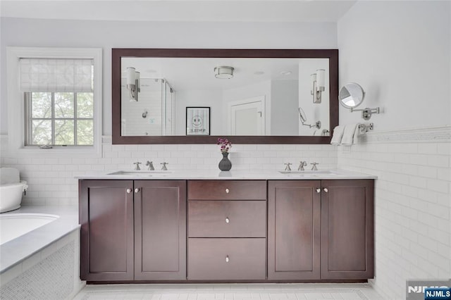 full bath with double vanity, tile walls, a stall shower, and a sink