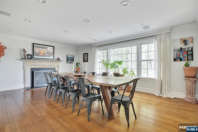 dining space with a fireplace with raised hearth, baseboards, ornamental molding, and light wood-style floors