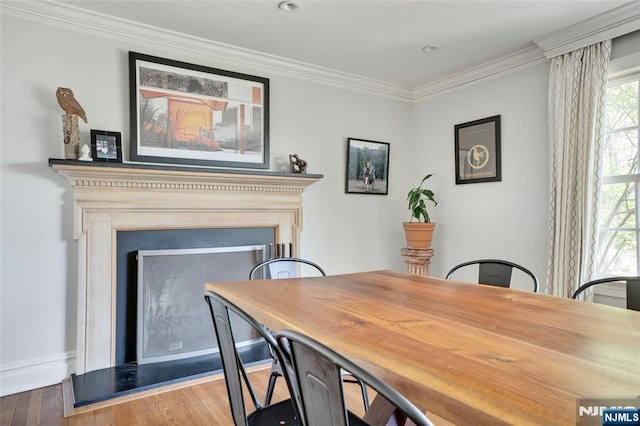 dining space featuring crown molding, a fireplace with raised hearth, baseboards, and wood finished floors