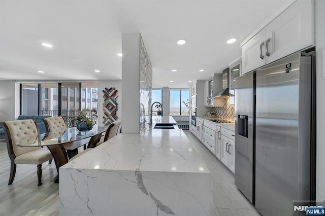 kitchen with a sink, stainless steel appliances, wall chimney exhaust hood, and a wealth of natural light