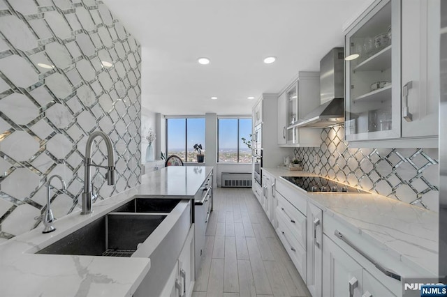 kitchen featuring backsplash, light stone countertops, black electric cooktop, a sink, and wall chimney exhaust hood