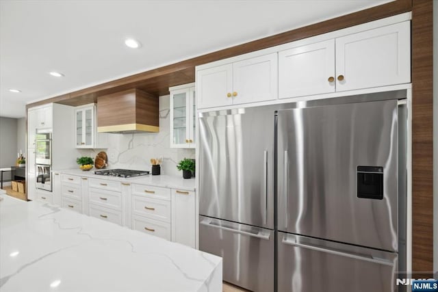kitchen featuring white cabinets, appliances with stainless steel finishes, glass insert cabinets, and custom range hood