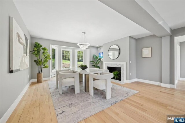 dining space with baseboards, light wood-style floors, a fireplace, and an inviting chandelier