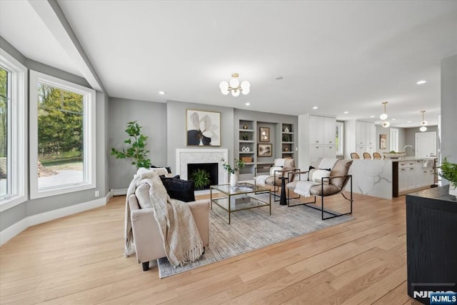 living room featuring an inviting chandelier, a fireplace, baseboards, recessed lighting, and light wood finished floors