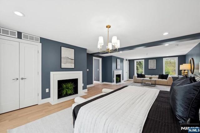 bedroom featuring a notable chandelier, recessed lighting, a fireplace with flush hearth, light wood-type flooring, and visible vents