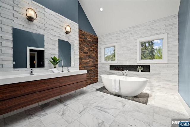 bathroom featuring double vanity, marble finish floor, a freestanding tub, high vaulted ceiling, and a sink