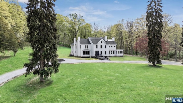 colonial inspired home featuring a view of trees, a chimney, and a front yard