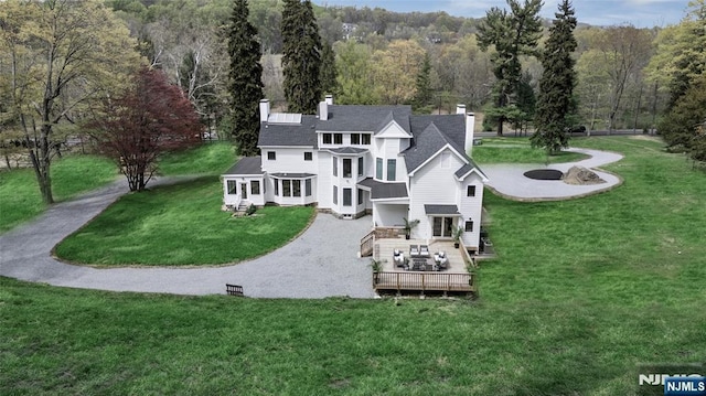 rear view of house featuring a yard, a deck, a view of trees, and a chimney