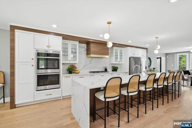 kitchen featuring white cabinets, stainless steel appliances, light wood-type flooring, a spacious island, and custom exhaust hood