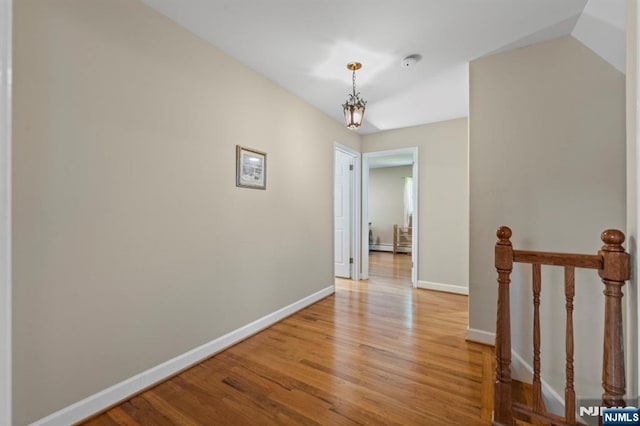 hall with baseboards, a notable chandelier, light wood finished floors, and an upstairs landing
