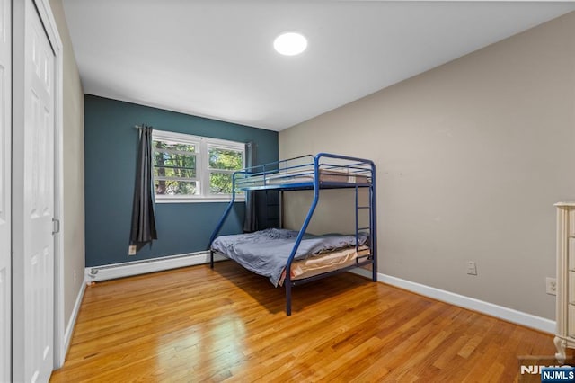 bedroom with baseboards, a baseboard radiator, wood finished floors, and a closet