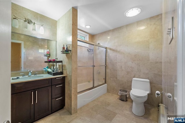 full bath with tile walls, tile patterned floors, bath / shower combo with glass door, vanity, and toilet