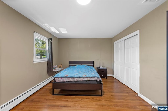 bedroom with visible vents, wood finished floors, baseboards, a baseboard radiator, and a closet