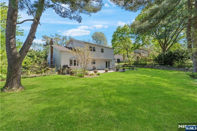 rear view of house with a chimney, a yard, and a patio area