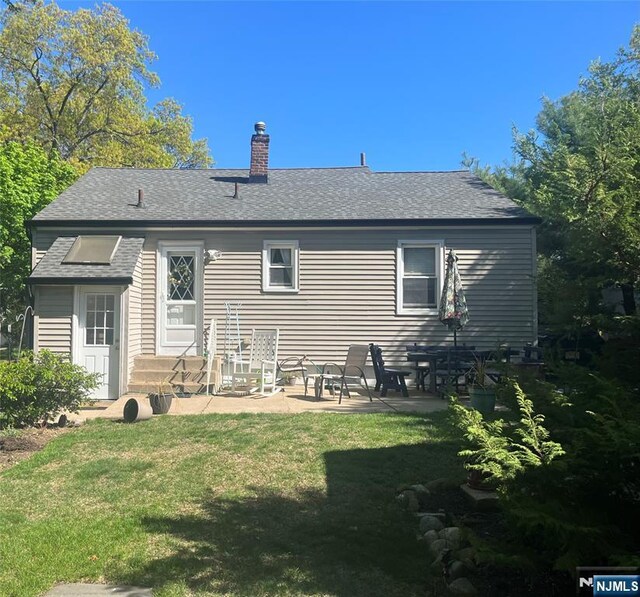 rear view of property with a lawn, roof with shingles, a chimney, and a patio