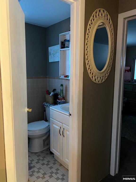 68 Echo Pl, Elmwood Park, NJ 07407 - bathroom featuring vanity, toilet, tile patterned floors, a wainscoted wall, and tile walls