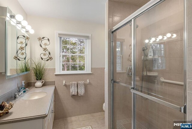 full bathroom featuring tile patterned flooring, vanity, toilet, tile walls, and a stall shower