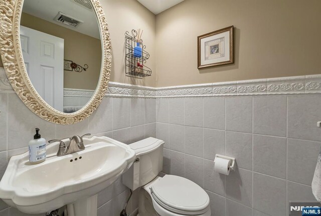 bathroom featuring a sink, tile walls, toilet, and visible vents