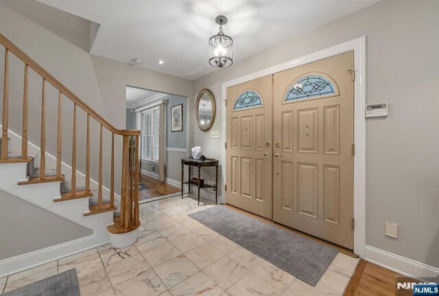foyer with stairs, baseboards, a chandelier, and marble finish floor