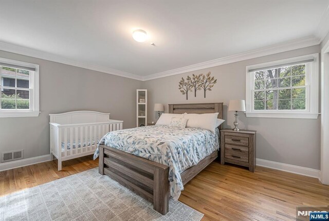bedroom featuring baseboards, visible vents, ornamental molding, and light wood finished floors