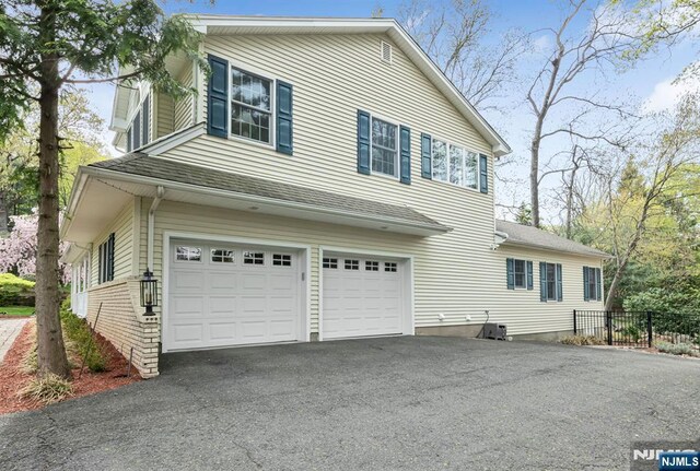 view of property exterior featuring a garage, fence, and driveway