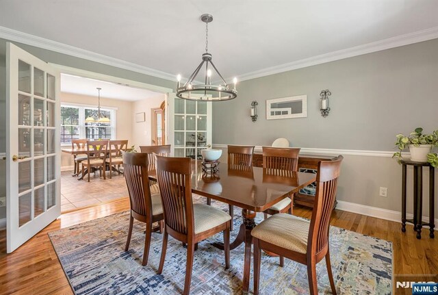dining space with an inviting chandelier, ornamental molding, light wood-style flooring, and baseboards