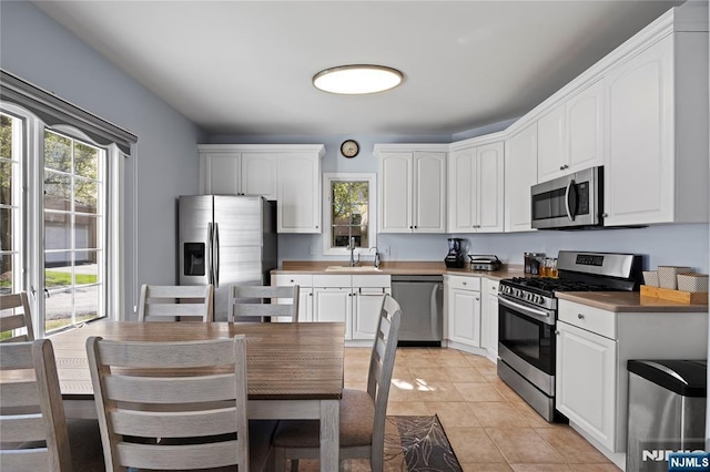 kitchen with a sink, light tile patterned floors, white cabinets, and stainless steel appliances