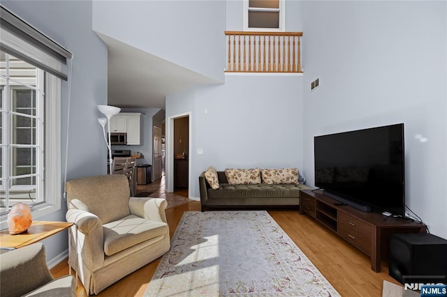living room featuring visible vents, light wood-style floors, a towering ceiling, and baseboards