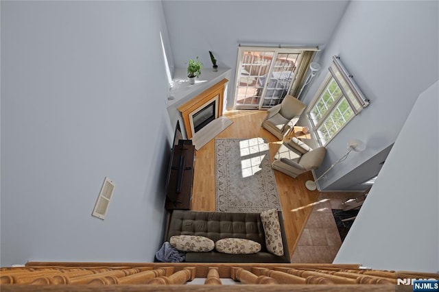 living room with a towering ceiling, a glass covered fireplace, and wood finished floors