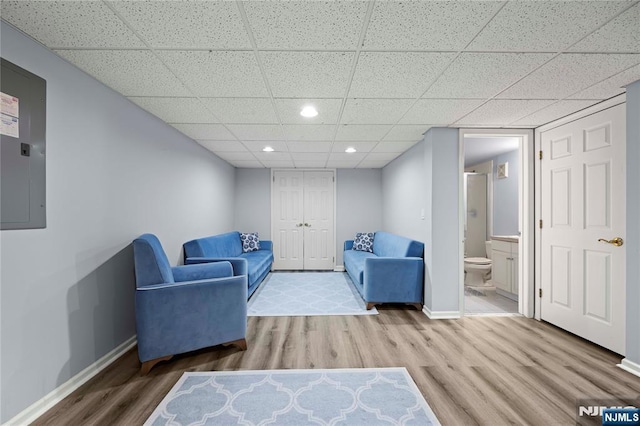 living area with electric panel, wood finished floors, baseboards, a drop ceiling, and recessed lighting