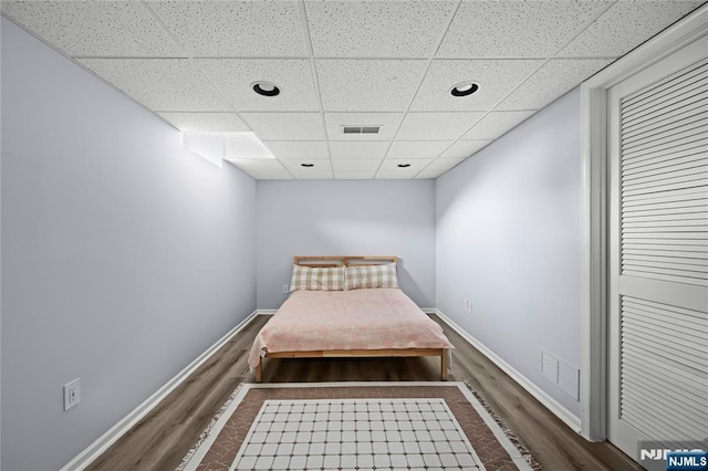 bedroom featuring baseboards, a drop ceiling, wood finished floors, and visible vents