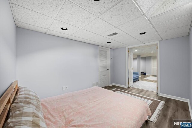 bedroom featuring baseboards, visible vents, a drop ceiling, and wood finished floors