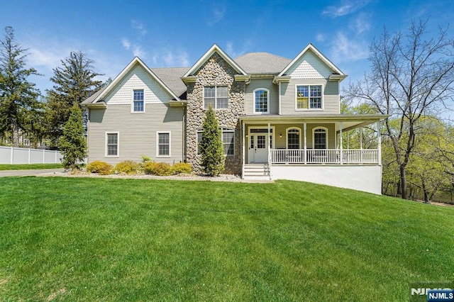 view of front of home with a porch, fence, stone siding, and a front yard