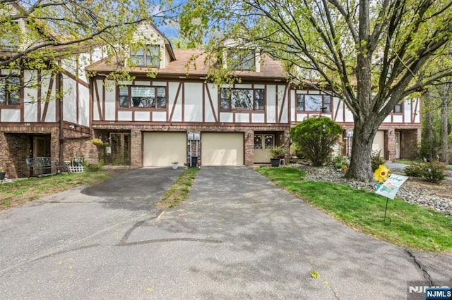tudor home featuring an attached garage, stucco siding, driveway, and brick siding