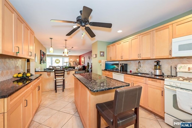 kitchen with light brown cabinetry, a breakfast bar, a sink, white appliances, and tasteful backsplash