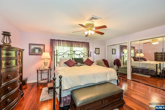 bedroom featuring multiple closets, visible vents, dark wood-style floors, and ceiling fan