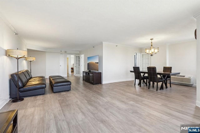 living room featuring baseboards, an inviting chandelier, a wall mounted air conditioner, and light wood-type flooring