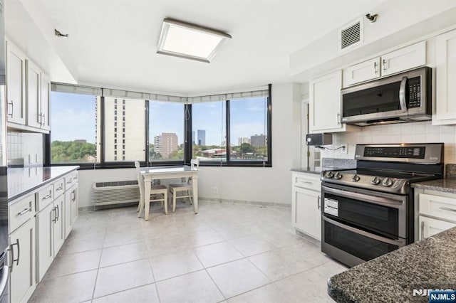 kitchen featuring decorative backsplash, visible vents, appliances with stainless steel finishes, baseboards, and dark stone counters