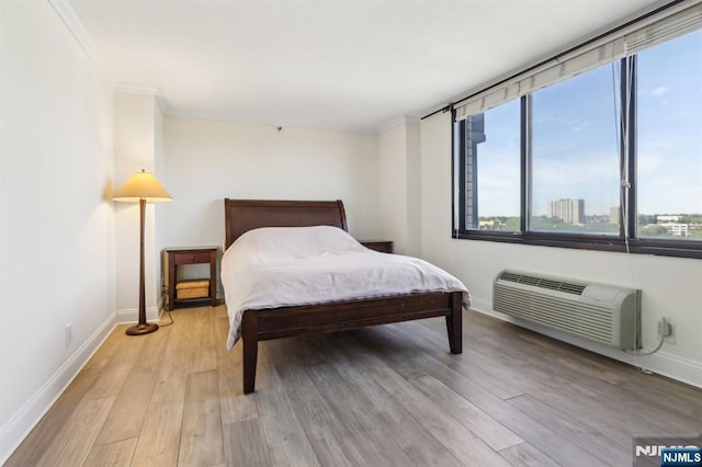 bedroom with baseboards, a wall unit AC, ornamental molding, and light wood finished floors