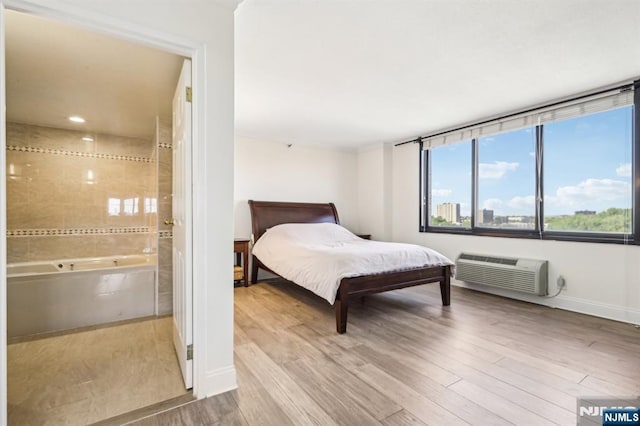 bedroom with connected bathroom, an AC wall unit, baseboards, and wood finished floors