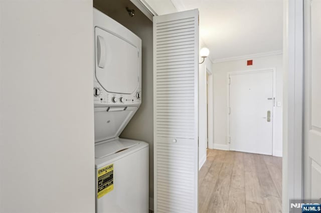 clothes washing area with crown molding, stacked washer / drying machine, light wood finished floors, and laundry area