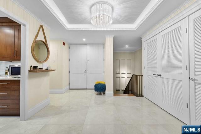corridor featuring crown molding, baseboards, a notable chandelier, and a raised ceiling