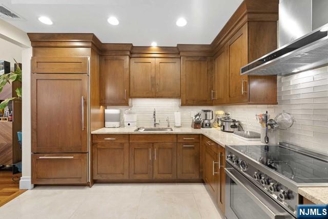 kitchen with a sink, wall chimney exhaust hood, backsplash, premium appliances, and visible vents