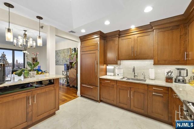 kitchen featuring backsplash, recessed lighting, brown cabinetry, and a sink